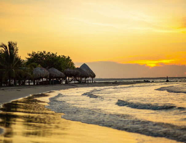 Vista del atardecer sobre la playa de Coveñas, con cabañas al fondo y oleaje suave.